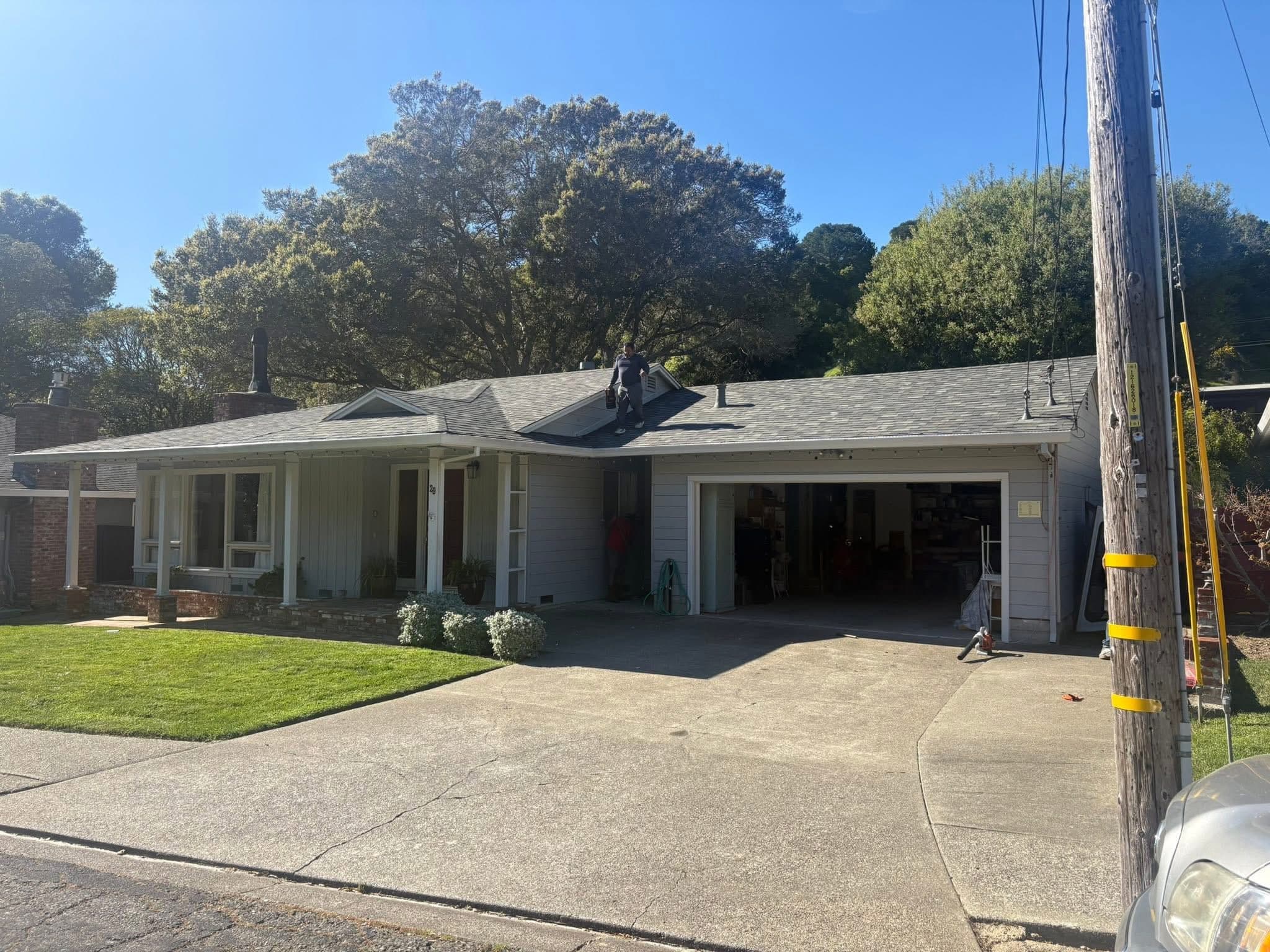 Person standing on the gray roof of a suburban house with an open garage.