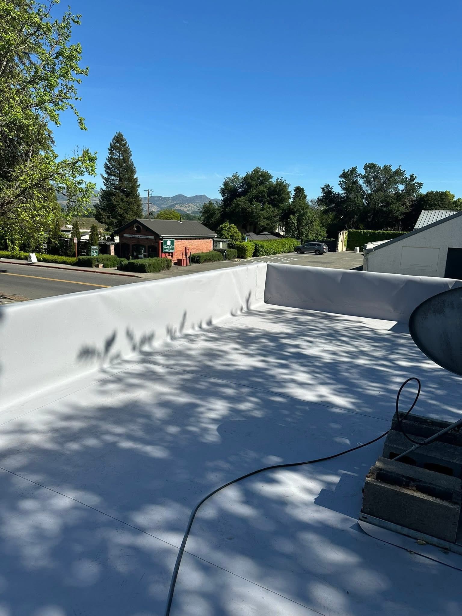 White flat roof with tree shadows, overlooking a street, brick building, and distant mountains.