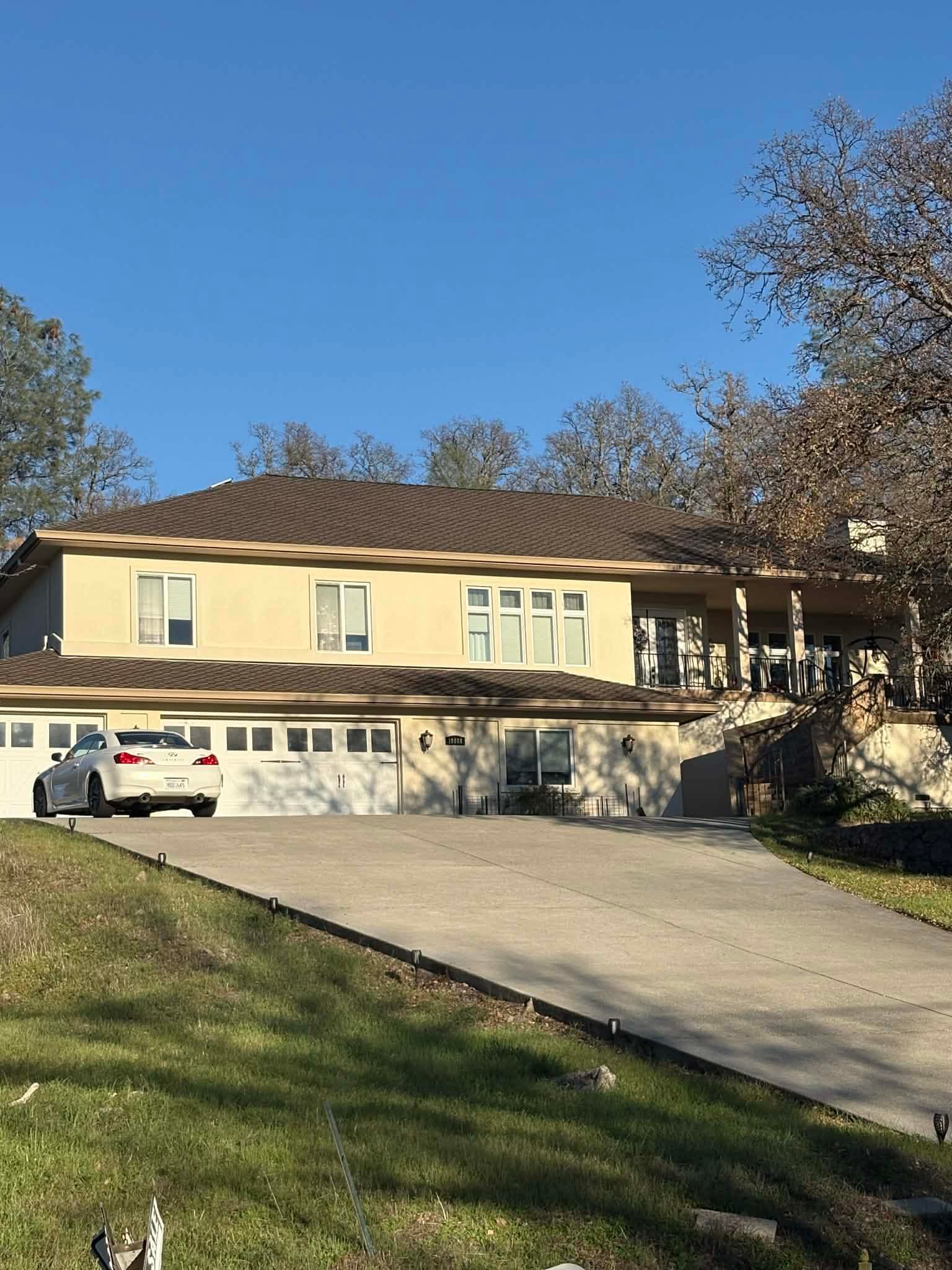 Large tan house with a brown roof and a white car in the long driveway.
